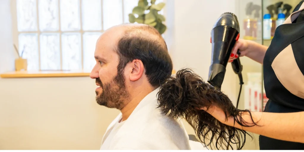 Barber drying a male hair system before fitting it on a client with thinning hair.